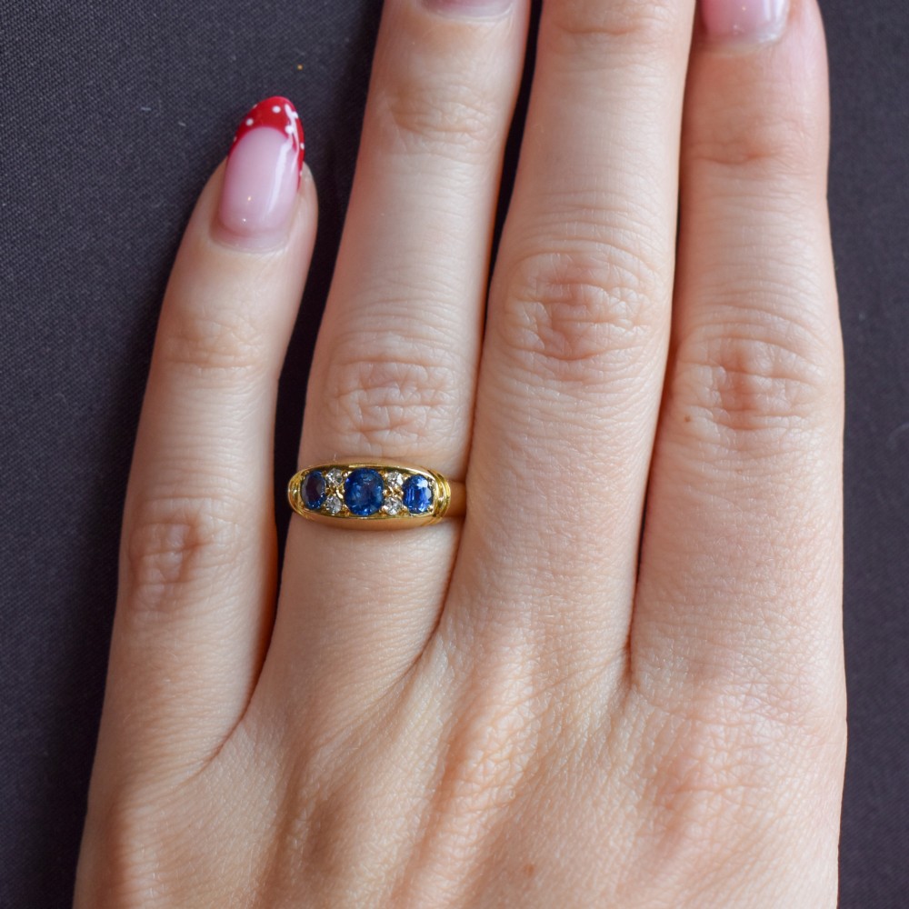 An Edwardian 18ct yellow gold boat ring set with three blue sapphires and accent diamonds in a carved setting. View X