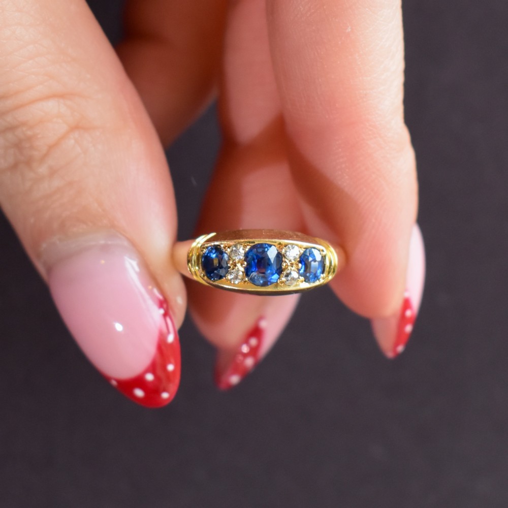 An Edwardian 18ct yellow gold boat ring set with three blue sapphires and accent diamonds in a carved setting. View XI