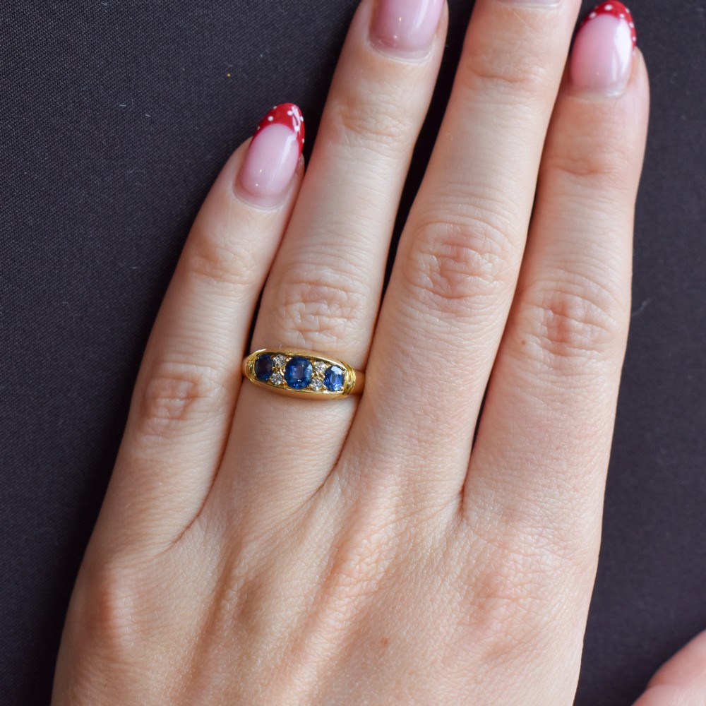 An Edwardian 18ct yellow gold boat ring set with three blue sapphires and accent diamonds in a carved setting. View XII