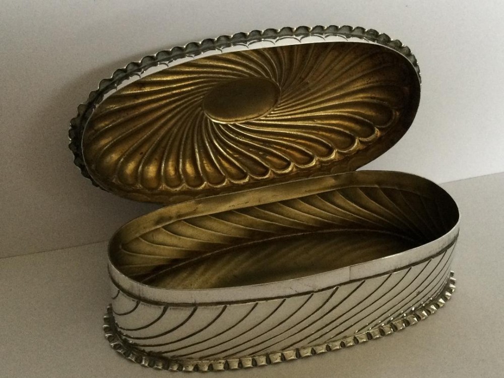An oval Victorian sterling silver snuff box shown open, featuring diagonal fluted reeding, a scalloped base, and a gilded interior.