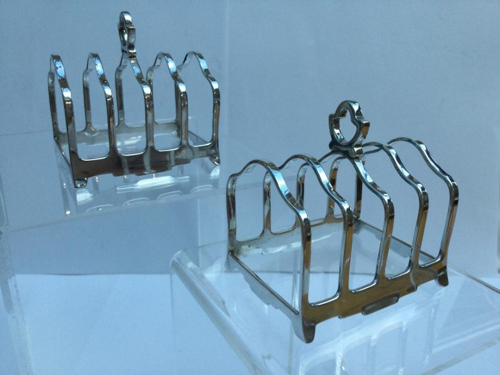 A pair of matching Art Deco silver toast racks featuring geometric central handles and four arched divisions on bracket feet.