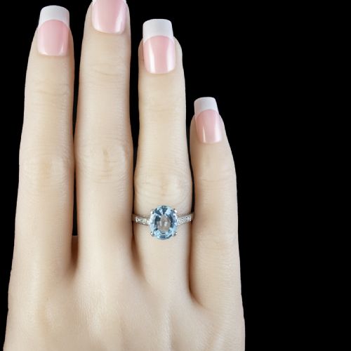 fig 3. An oval-cut light blue aquamarine gemstone set in a four-claw mount with channel-set diamond shoulders on a silver-coloured metal band.