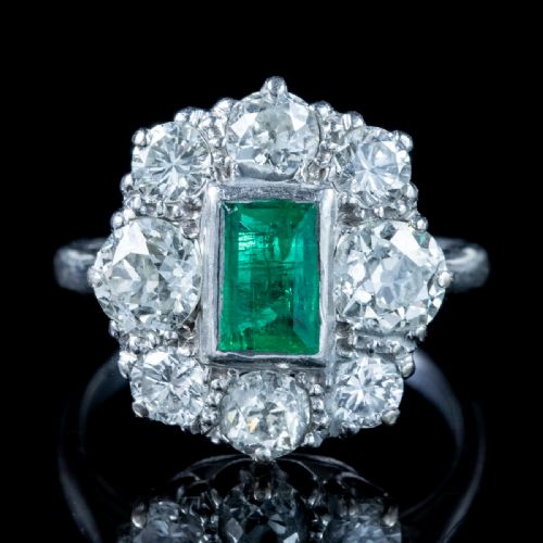 fig 1. An antique Edwardian cluster ring featuring a central rectangular step-cut green emerald framed by eight old-cut diamonds in a white metal setting.