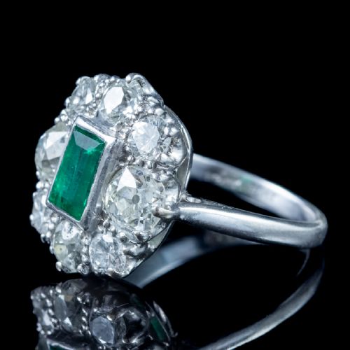 fig 2. An antique Edwardian cluster ring featuring a central rectangular step-cut green emerald framed by eight old-cut diamonds in a white metal setting.