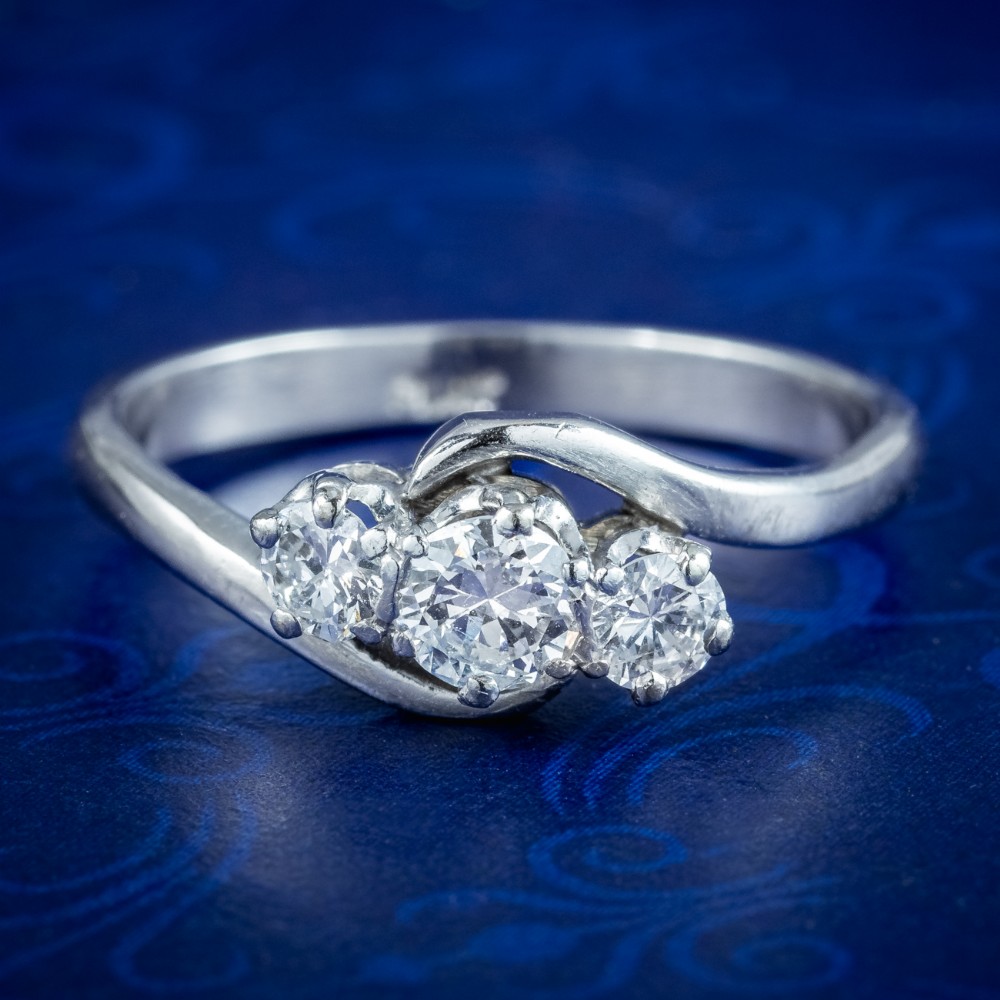 An Edwardian platinum trilogy ring featuring three round diamonds set in a crossover twist band.