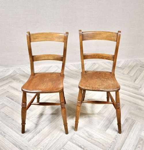 A pair of antique warm brown wooden barback kitchen chairs featuring solid contoured seats, double horizontal back rails, and turned legs. View II