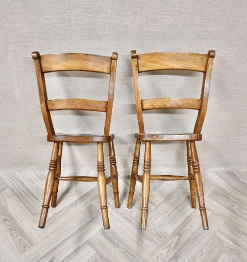 A pair of antique warm brown wooden barback kitchen chairs featuring solid contoured seats, double horizontal back rails, and turned legs. View IV