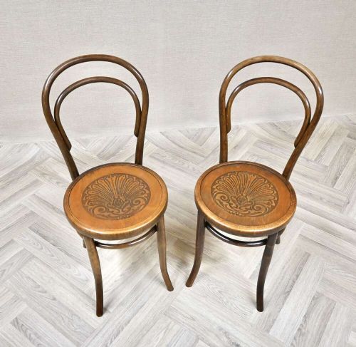 A pair of warm brown steam-bent beech side chairs featuring curved double-loop backs and embossed decorative shell designs on the circular plywood seats. View II