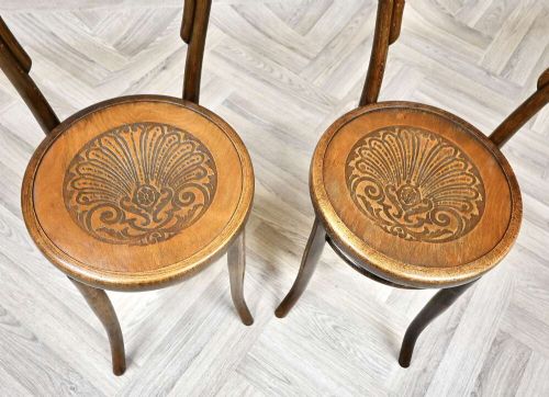 A pair of warm brown steam-bent beech side chairs featuring curved double-loop backs and embossed decorative shell designs on the circular plywood seats. View III