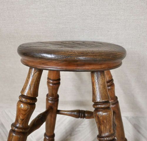 A nineteenth-century turned wooden Windsor stool featuring a circular polished seat supported by four splayed turned legs and turned stretchers. View V