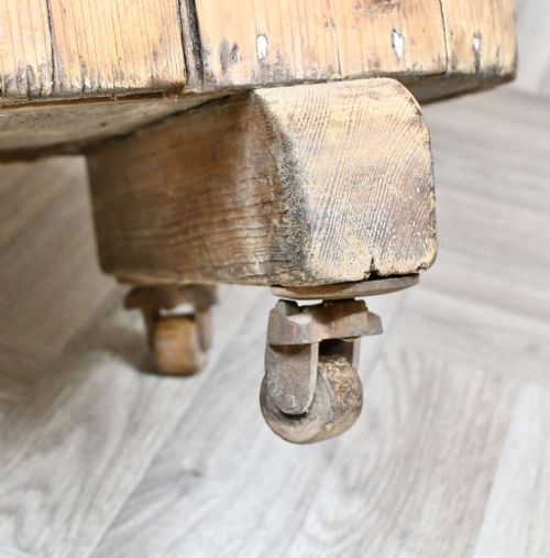 An antique natural pine huffer cupboard featuring a curved front, single panelled door with a brass knob, iron latch, side handles, and short wooden legs on metal castors. View V
