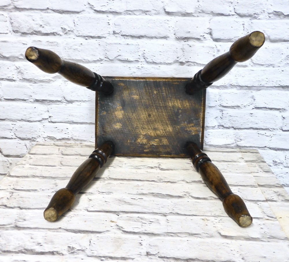 A low dark wooden hearth stool featuring a thick rectangular seat supported by four turned splayed legs. View V