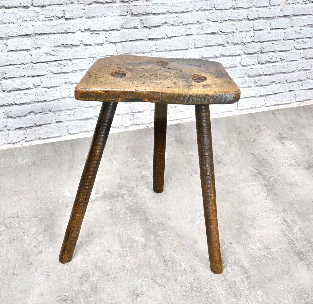 A 19th-century rustic three-legged wooden cutler stool featuring a thick shaped seat with visible tenon joints and splayed legs. View VIII