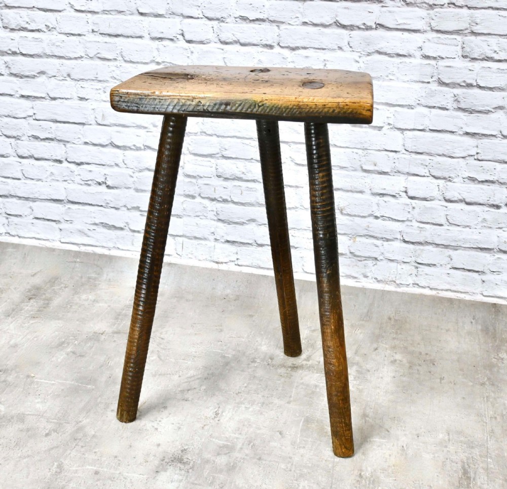 A 19th-century three-legged wooden cutlers stool featuring a thick rectangular top and splayed turned legs. View VII