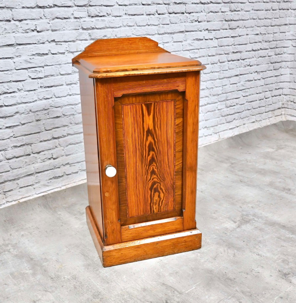 A tall Victorian pine bedside cupboard featuring a single door with prominent wood grain, a white ceramic knob, and a gallery top.