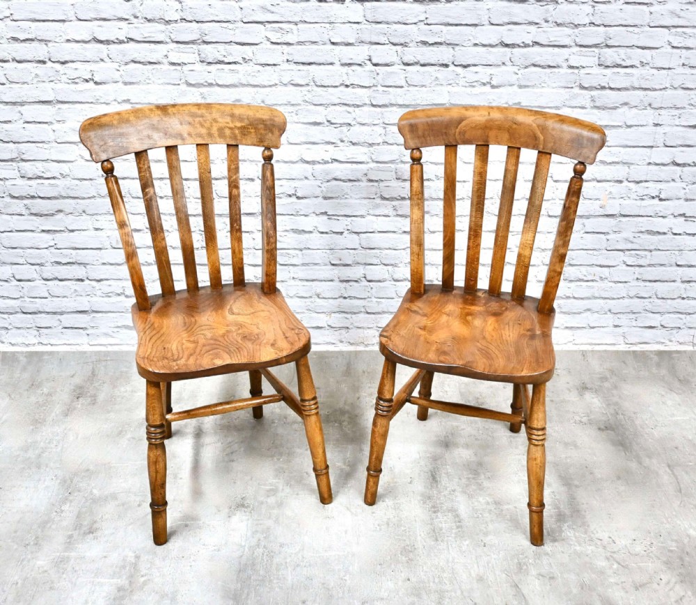 A pair of wooden Windsor kitchen chairs with lath backs, solid shaped seats, and turned legs.