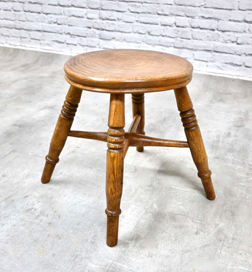 A low wooden country stool with a circular dished seat, four turned splayed legs, and a central cross stretcher. View VII