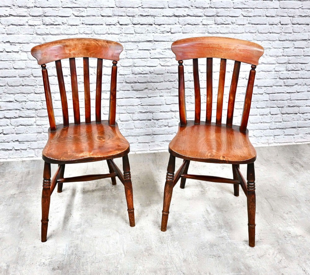 A pair of warm brown wooden country kitchen chairs featuring curved crest rails, vertical back slats, contoured seats, and turned legs. View VI