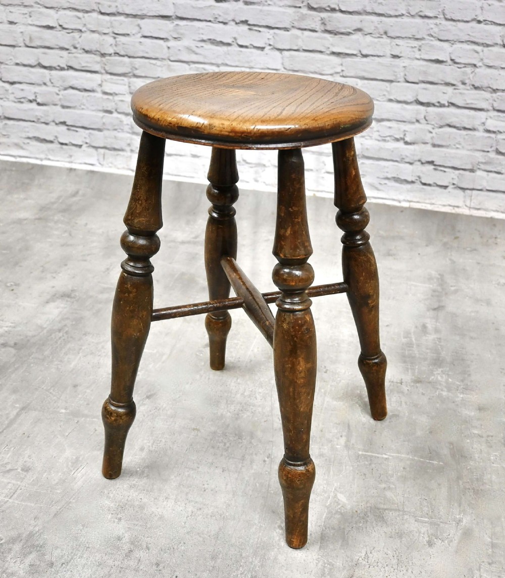 A circular dark wood Windsor stool with turned legs and an X-shaped cross stretcher.