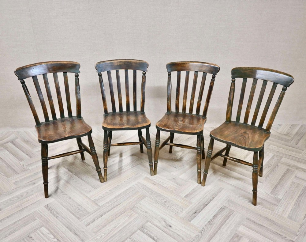 A set of four dark brown 19th-century wooden Windsor dining chairs featuring lath backrests, contoured seats, and turned legs.