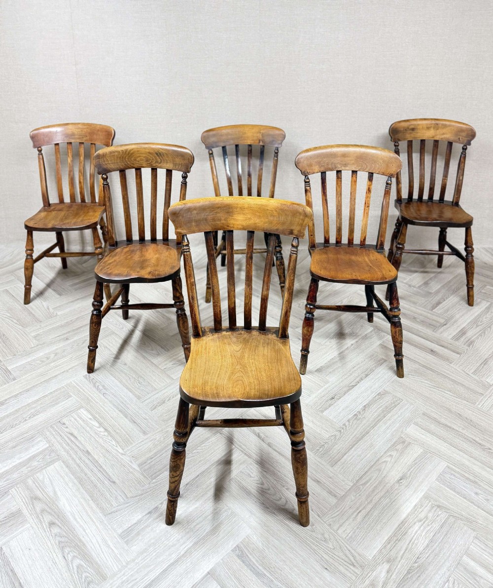 A set of six antique wooden country kitchen chairs featuring turned legs, vertical back spindles, and contoured timber seats.
