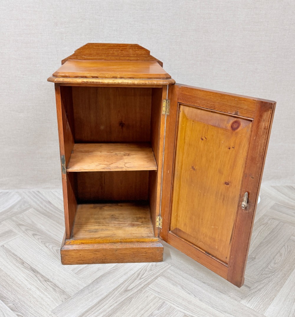 An antique pine pot cupboard featuring a single panelled door with a white ceramic knob, set on a solid plinth base. View III