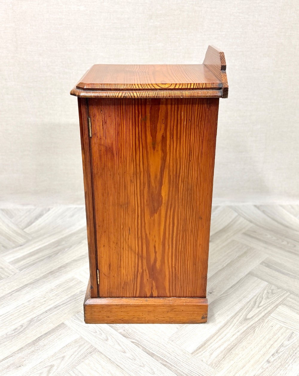An antique pine pot cupboard featuring a single panelled door with a white ceramic knob, set on a solid plinth base. View V