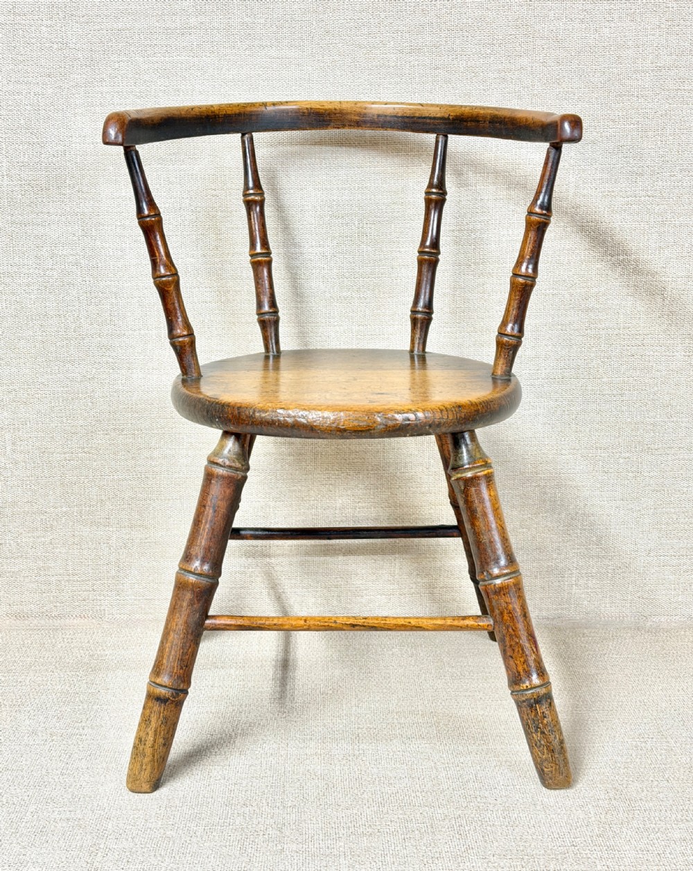 An antique dark wood childs Windsor chair featuring turned faux-bamboo spindles, a curved top rail, a solid wooden seat, and splayed turned legs with stretchers. View II