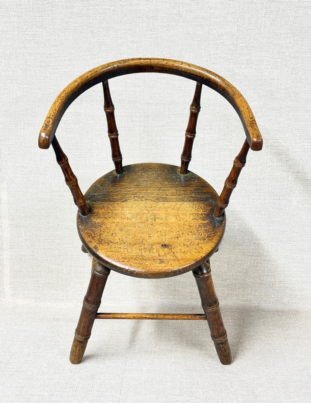 An antique dark wood childs Windsor chair featuring turned faux-bamboo spindles, a curved top rail, a solid wooden seat, and splayed turned legs with stretchers. View III