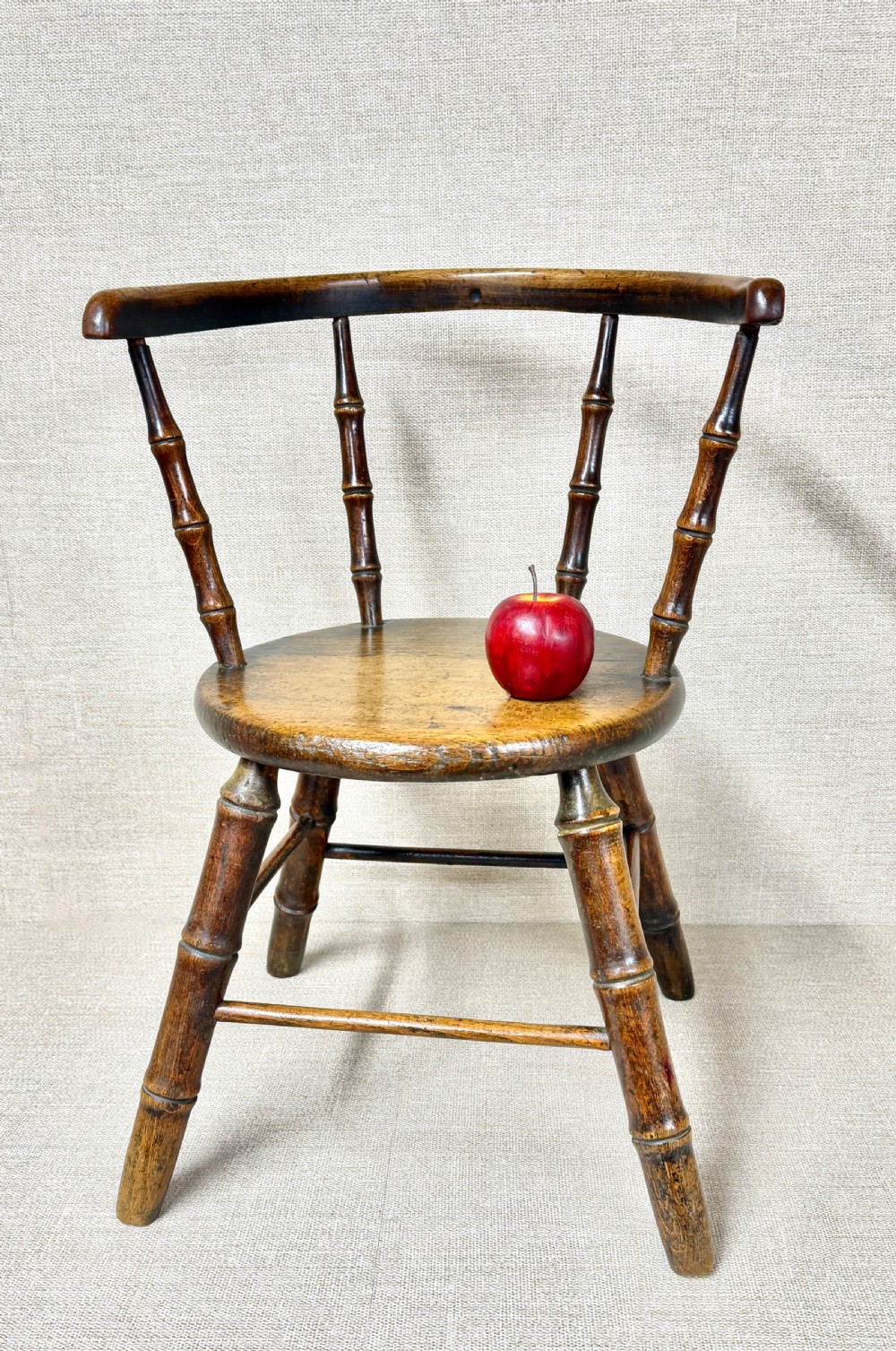 An antique dark wood childs Windsor chair featuring turned faux-bamboo spindles, a curved top rail, a solid wooden seat, and splayed turned legs with stretchers. View IV