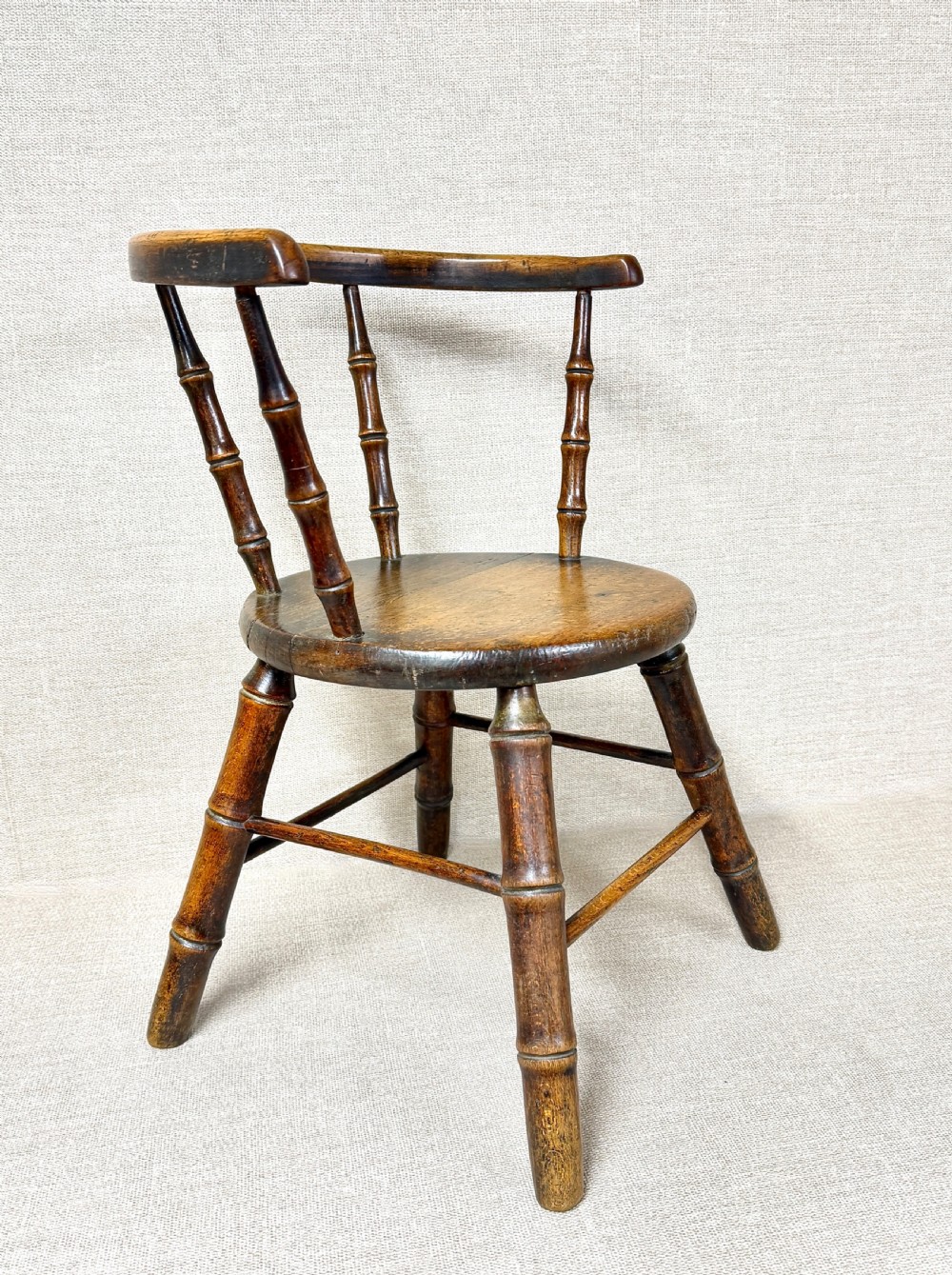 An antique dark wood childs Windsor chair featuring turned faux-bamboo spindles, a curved top rail, a solid wooden seat, and splayed turned legs with stretchers. View V