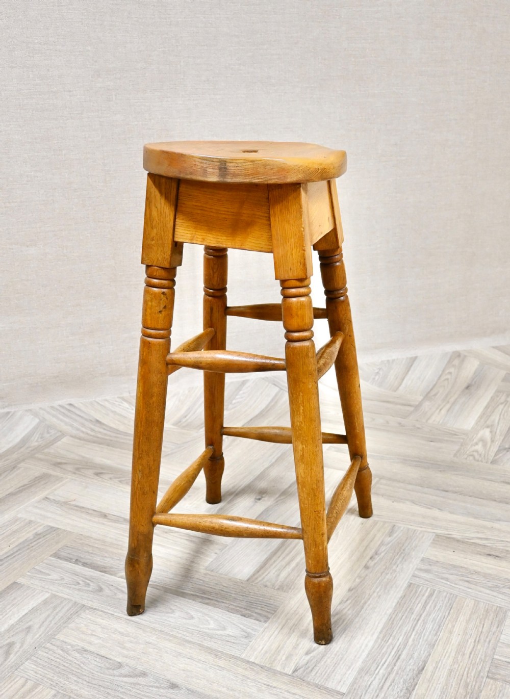 A tall 19th-century wooden bar stool featuring turned legs, lower footrest stretchers, and a rounded seat with a carved handhold slot. View II
