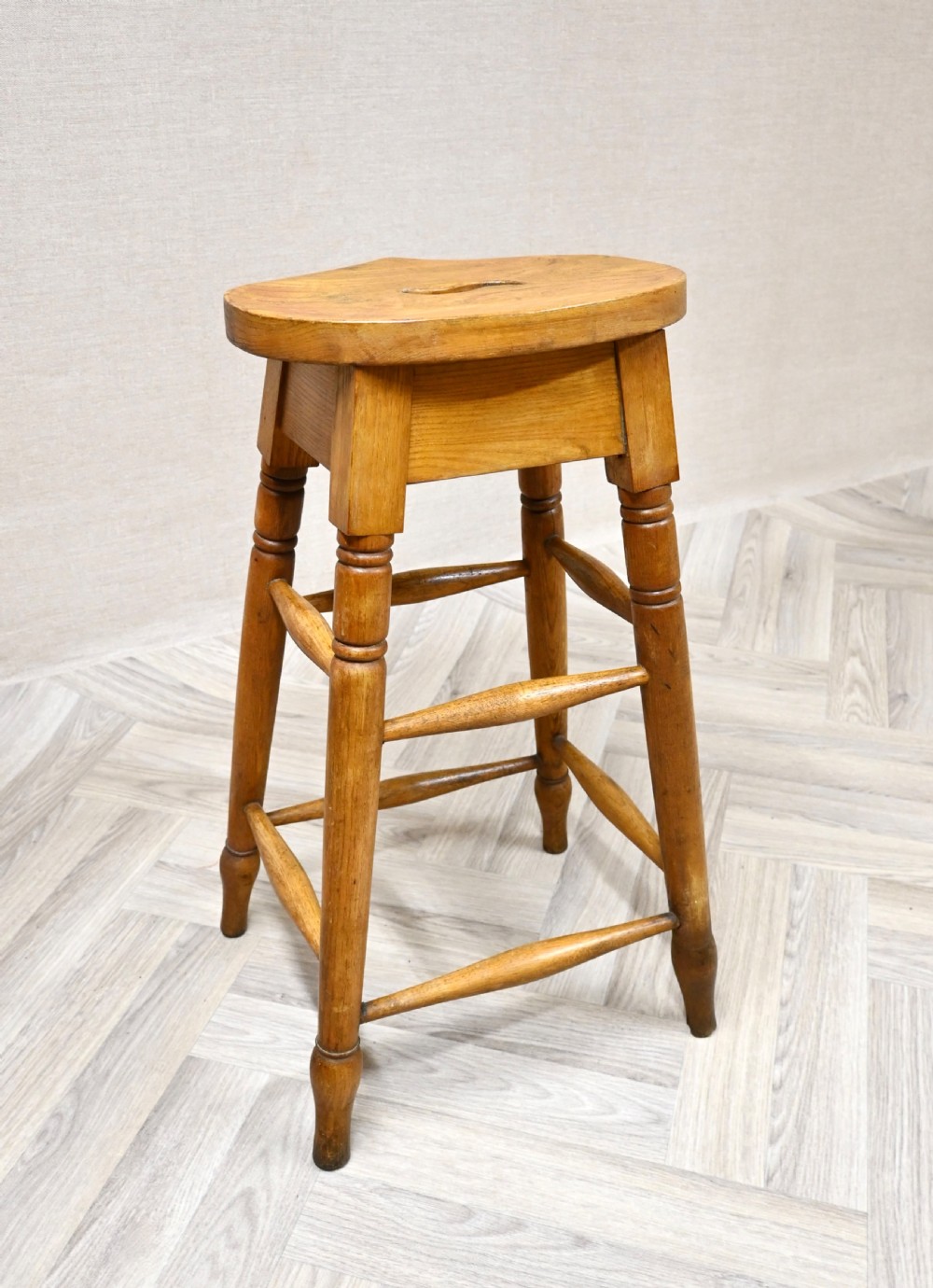 A tall 19th-century wooden bar stool featuring turned legs, lower footrest stretchers, and a rounded seat with a carved handhold slot. View IV