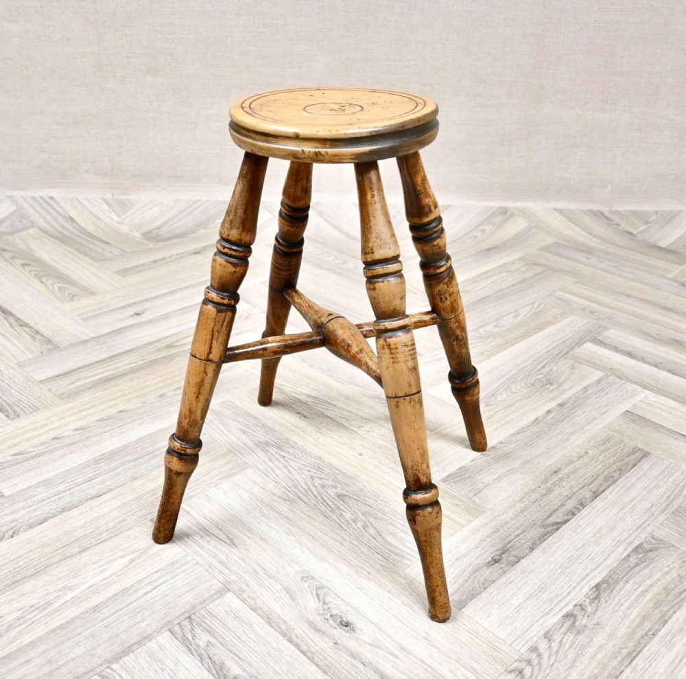 A 19th-century wooden country stool featuring four turned legs, cross stretchers, and a circular seat with incised concentric grooves. View VII