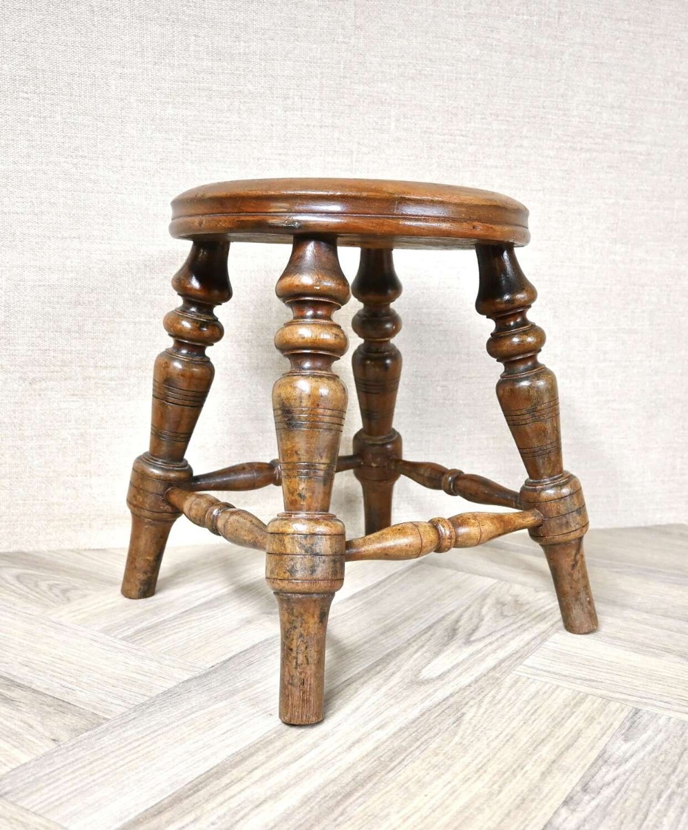 A 19th-century dark wooden nursery stool featuring baluster turned legs, horizontal stretchers, and a circular solid wood top.