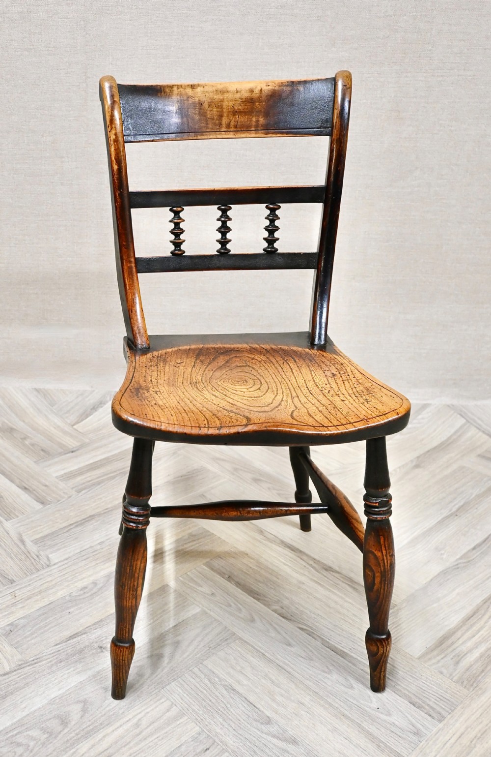 A set of four 19th-century wooden Windsor kitchen dining chairs featuring shaped elm seats, bar backs with spindle details, turned legs, and H-stretchers. View II