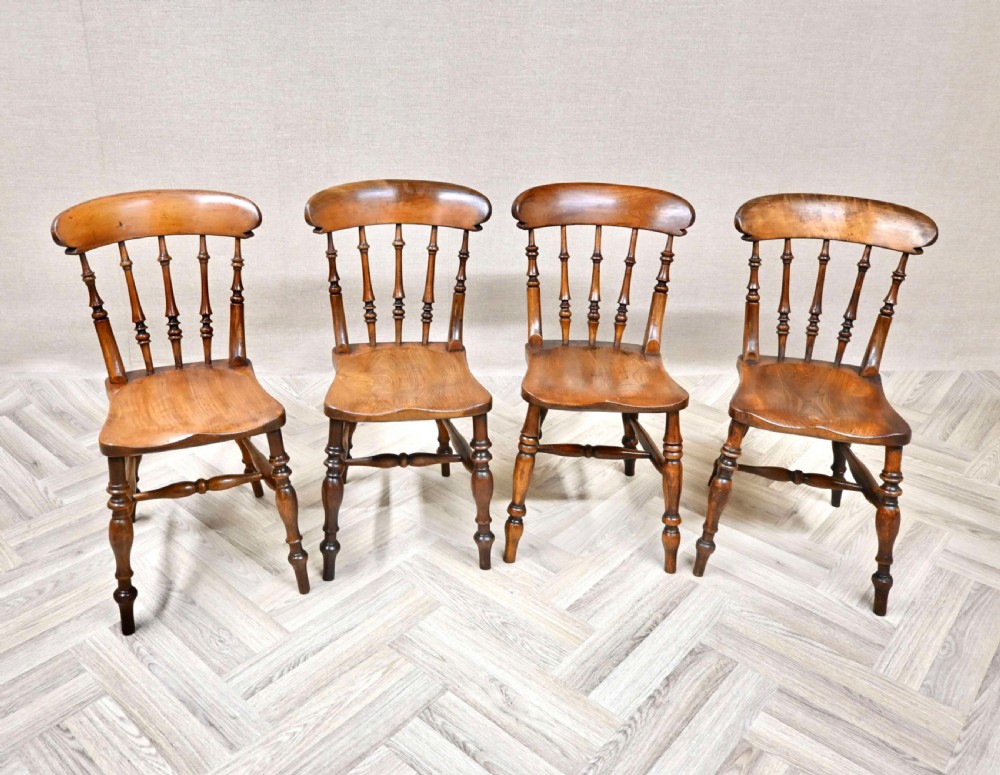 A set of four antique wooden Windsor dining chairs featuring shaped top rails, turned spindles, saddle seats, and stretchered legs.