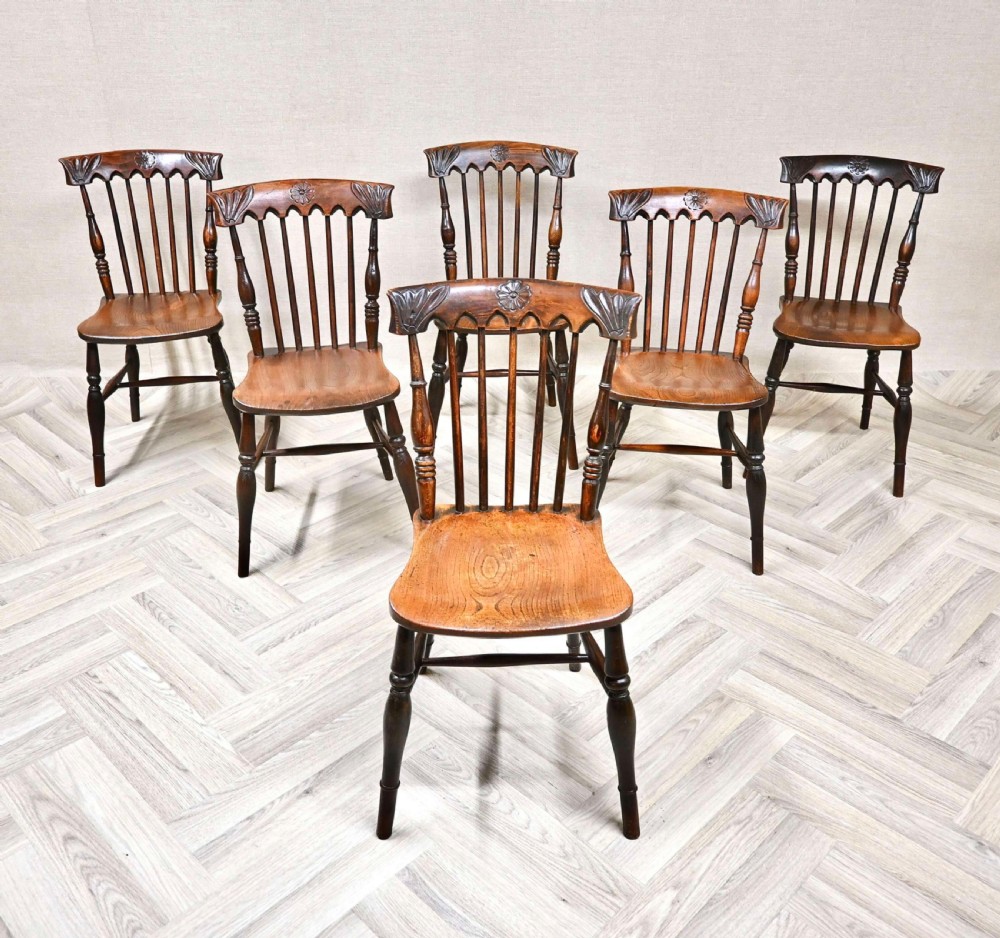 A set of six antique wooden Windsor dining chairs featuring carved crest rails, spindle backrests, shaped wooden seats, and turned legs.
