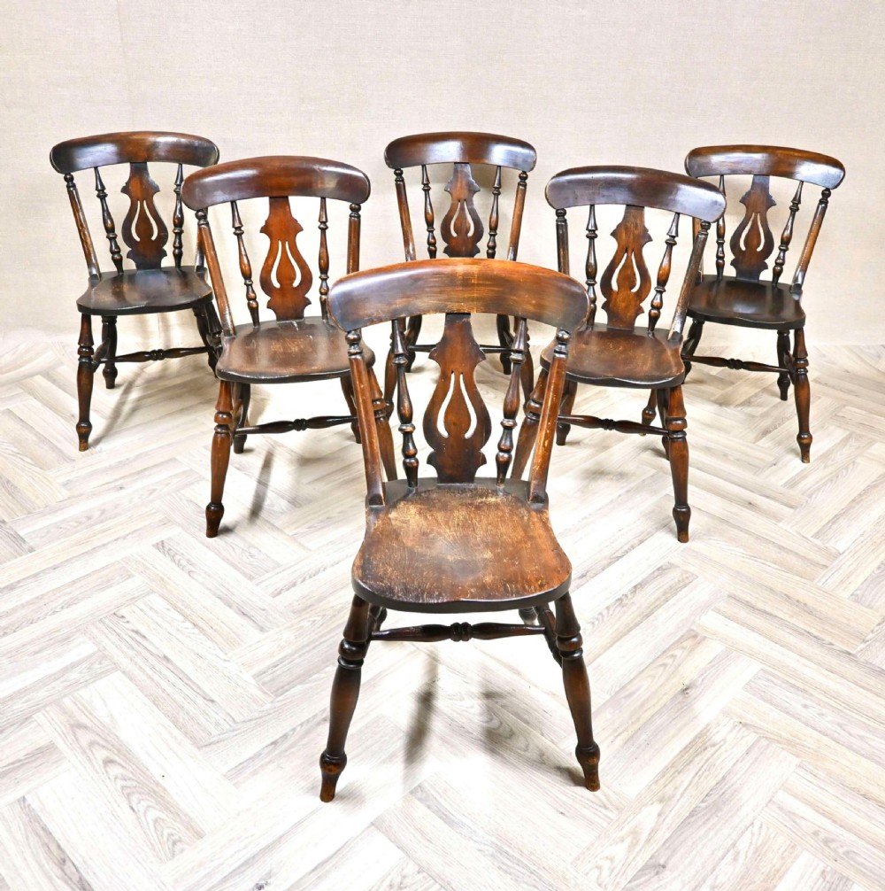 A matching set of six dark brown antique Windsor kitchen chairs featuring pierced back splats, turned spindles, and solid wooden seats.