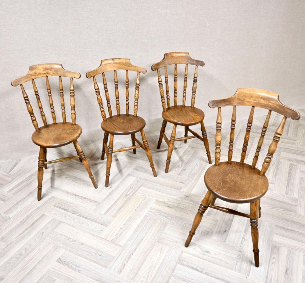 A set of four warm brown wooden Windsor chairs featuring circular penny seats, turned back spindles, and turned legs.