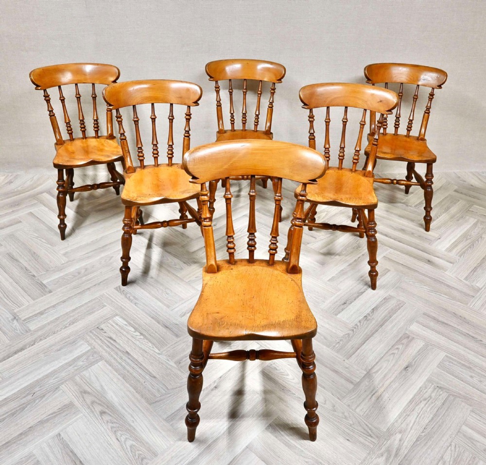 A set of six matching wooden Windsor dining chairs featuring turned back spindles, curved crest rails, shaped saddle seats, and turned legs.