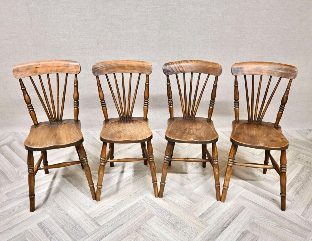 A set of four Edwardian wooden Windsor kitchen chairs with fan back spindles, shaped seats, and turned legs.