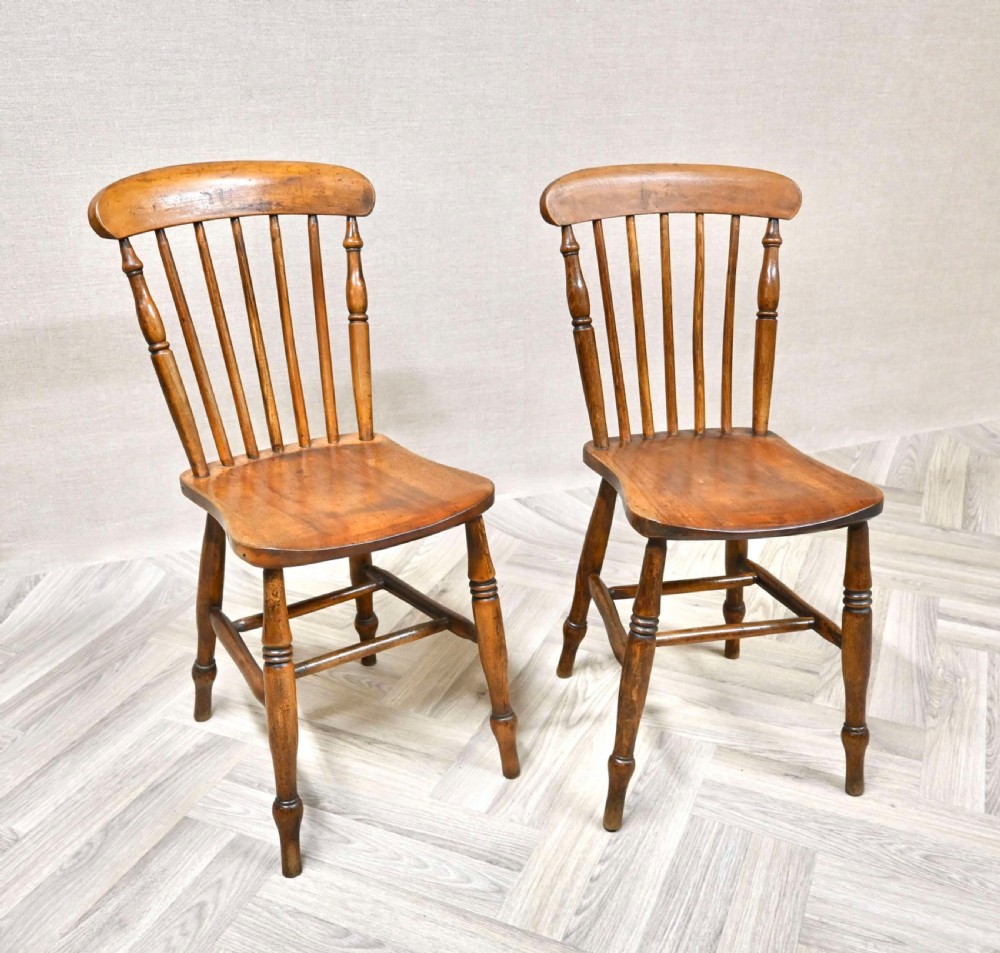 A pair of antique wooden Windsor dining chairs featuring spindle backrests, curved top rails, solid contoured seats, and turned legs with stretchers.