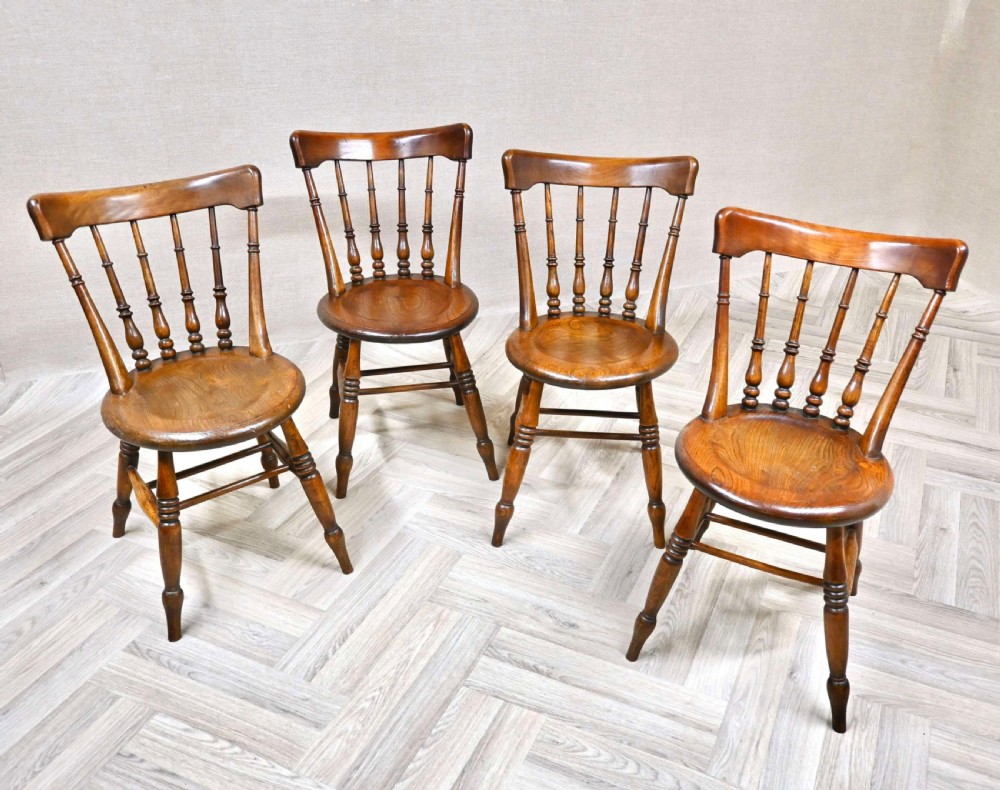 A set of four warm brown wooden Windsor dining chairs featuring circular penny seats, turned back spindles, and turned legs with stretchers.