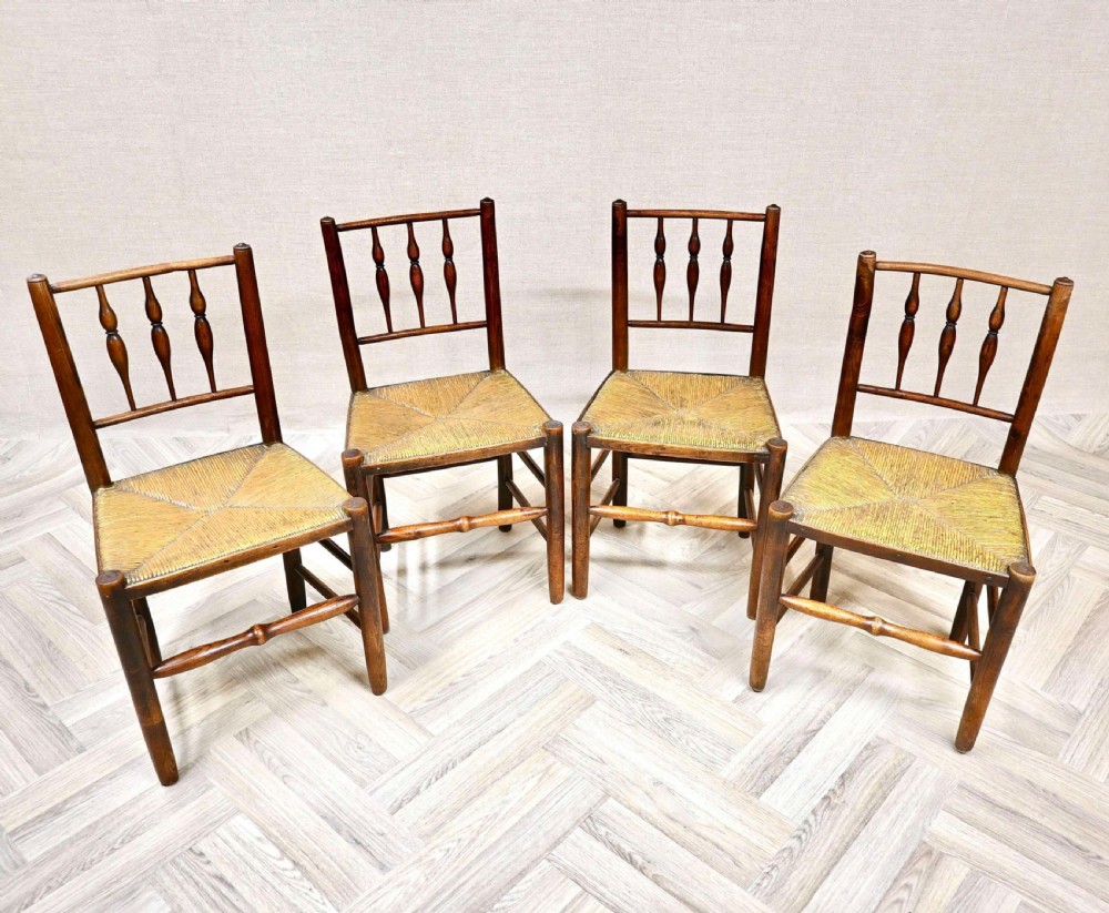 A set of four dark timber country dining chairs featuring turned spindle backs and hand-woven rush seats.