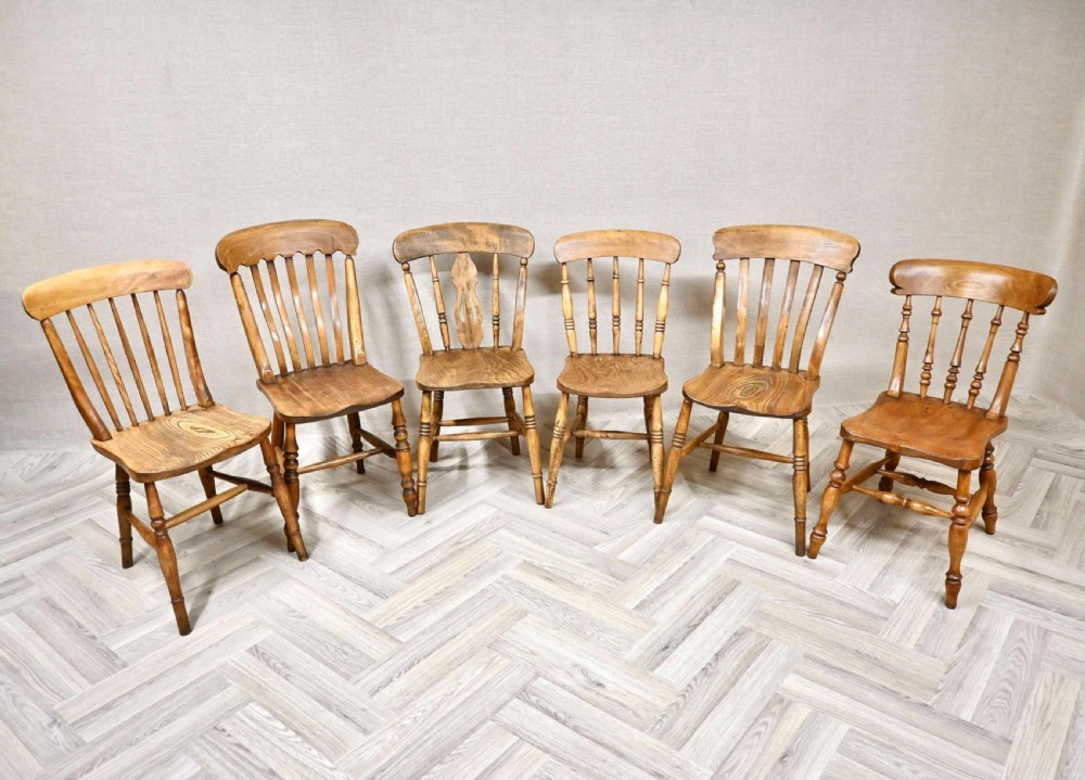 A set of six wooden Windsor dining chairs featuring stick backs, saddle seats, turned legs, and stretchers.