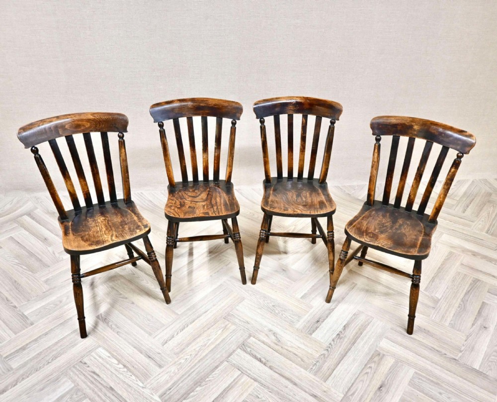 A set of four antique dark wood Windsor dining chairs featuring vertical lath backs, solid shaped seats, and turned legs with stretchers.