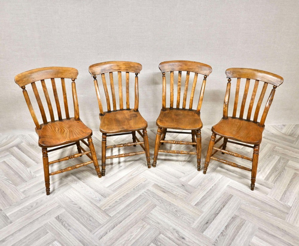 A set of four golden brown wooden Windsor lathback dining chairs with curved top rails, vertical slats, contoured seats, and turned legs.