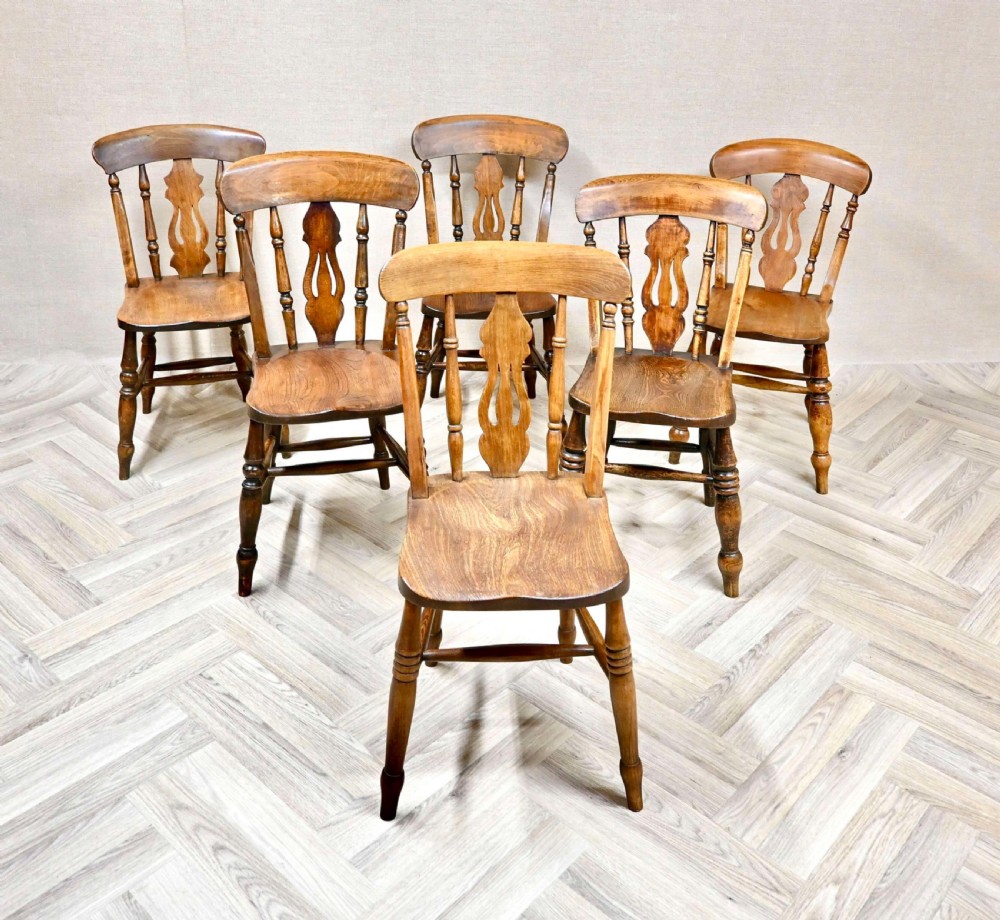 A set of six antique wooden country kitchen chairs featuring curved top rails, central decorative splats, turned legs, and solid timber seats.