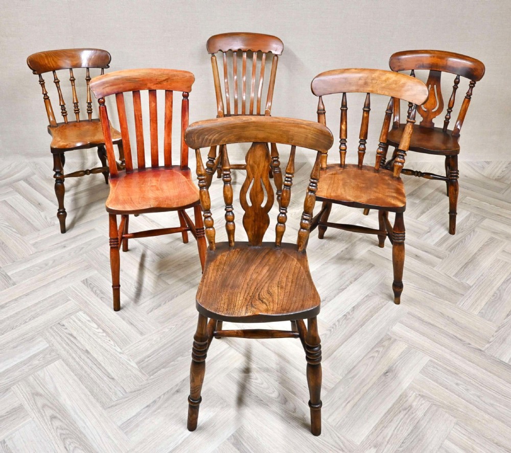 A set of six warm brown wooden country kitchen chairs featuring turned legs, solid seats, and varied spindle and splat backs.